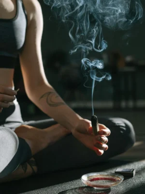 A person practicing meditation holding burning incense with smoke rising gently.