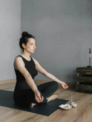 A woman in a serene pose meditates indoors, surrounded by candles and incense, symbolizing relaxation.