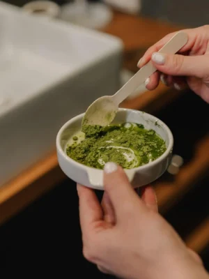 Close-up of a woman blending a green skincare mask in a stylish indoor setting.