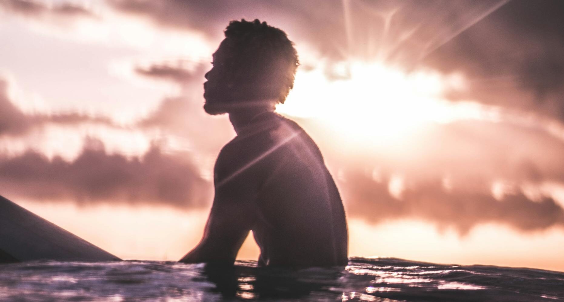 Silhouette of a serene surfer in the ocean at sunset, capturing a peaceful and idyllic moment.
