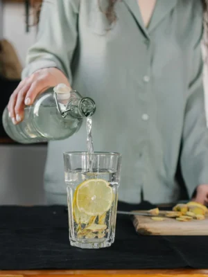 Woman pours water for lemon ginger infusion, promoting health and hydration.